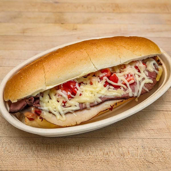 A Roundabout Pizza sub sandwich with roast beef, melted cheese, and diced tomatoes in a white dish.