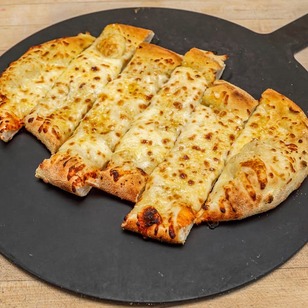 Roundabout Pizza's cheesy breadsticks, golden brown and cut into strips, on a dark pizza peel.