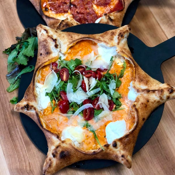 Roundabout Pizza's star-shaped pizza with arugula, cherry tomatoes, and shaved parmesan, with a pepperoni pizza in the background.
