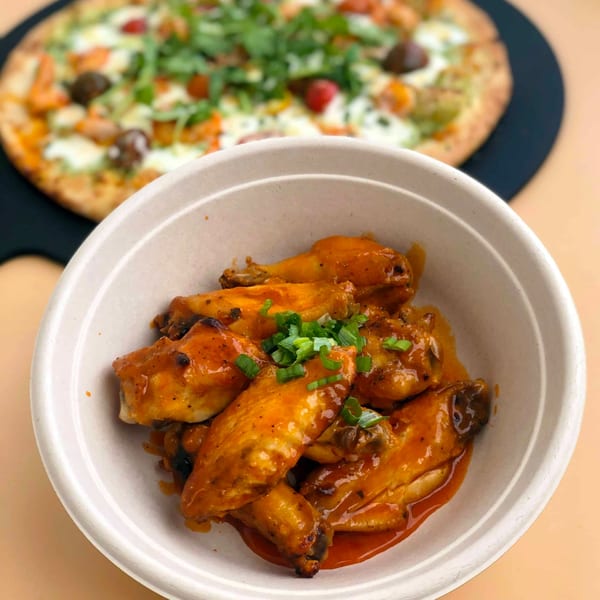 Roundabout Pizza's buffalo wings in a bowl with a blurred pizza in the background.