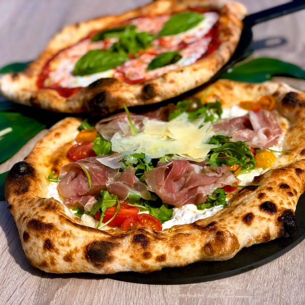 Two Roundabout pizzas: one with prosciutto, arugula, and shaved parmesan, another with basil and mozzarella.